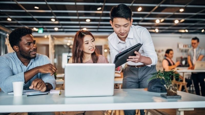 Group collaborating in office, man using laptop, conveying teamwork and productivity