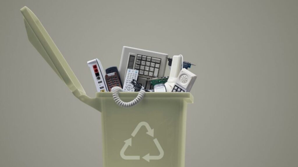 Recycling bin filled with discarded electronics like keyboard and phones, promoting e-waste recycling.