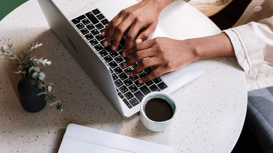 Hands on a keyboard with a cup of coffee nearby