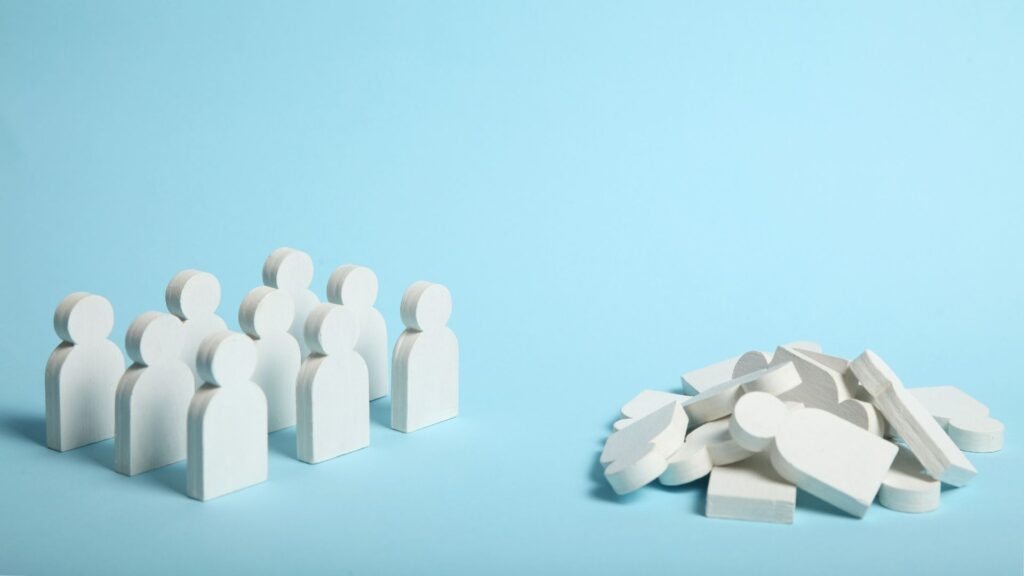 A group of carved wooden figures stand upright next to a pile of disassembled wooden figures. The background is blue