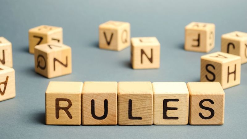 Wooden letter cubes arranged to spell out the word "RULES" on a gray surface, representing guidelines or regulations