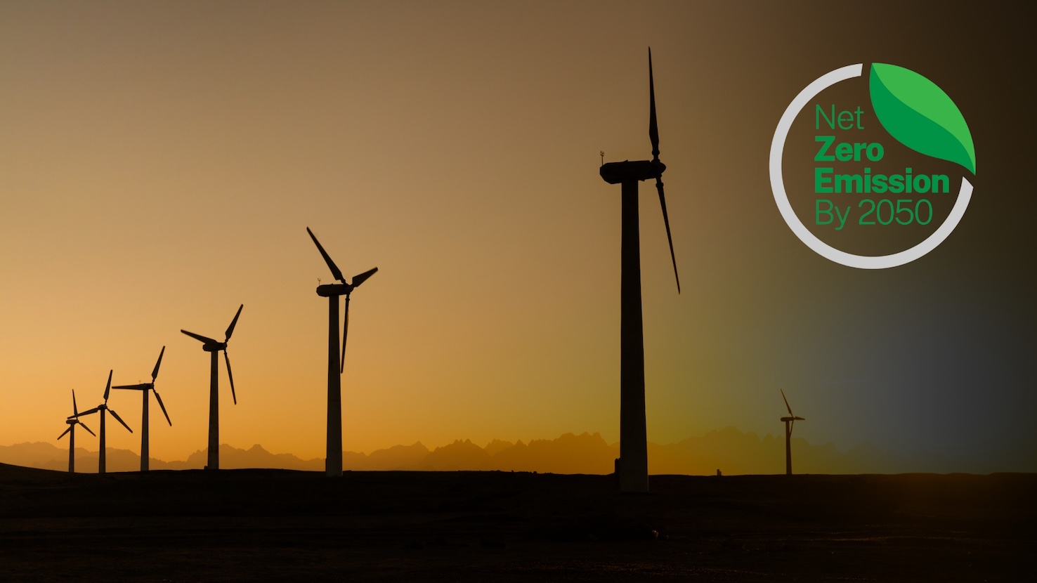 Silhouette of wind turbines against a sunset sky, with a green leaf icon and the text "Net Zero Emission By 2050