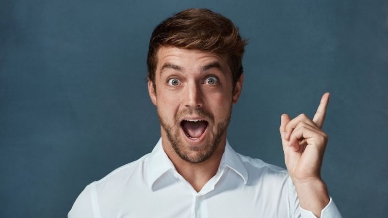 Surprised man in a white shirt pointing upwards with one finger against a dark blue background