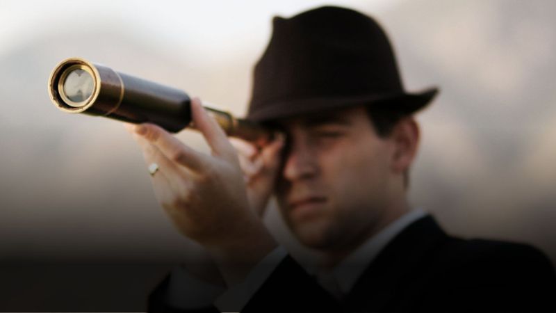 Man in a hat looking through a vintage telescope