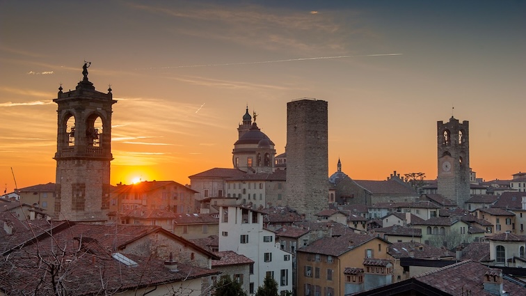 A panoramic view of Bergamo, Italy, at sunset, featuring historic buildings and a dramatic sky