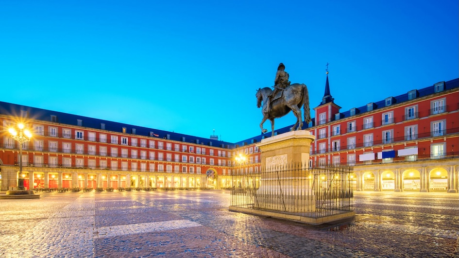 A historic square in Madrid, Spain, at night, featuring a statue of King Philip III and illuminated buildings