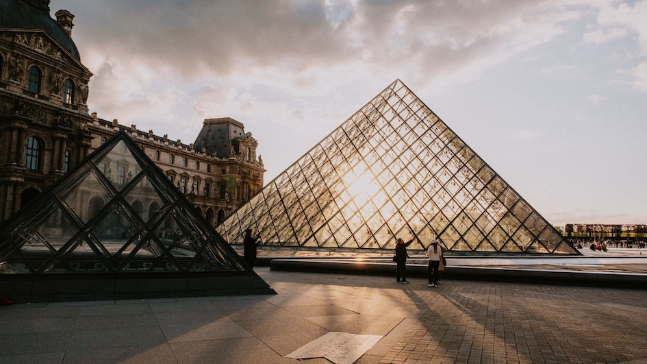 The iconic glass pyramid entrance to the Louvre Museum in Paris, France, with the museum's historic building in the background